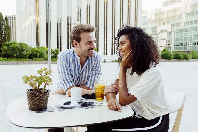 Романтическая многорасовая пара, сидящая вместе в кафе на открытом воздухе — стоковое фото