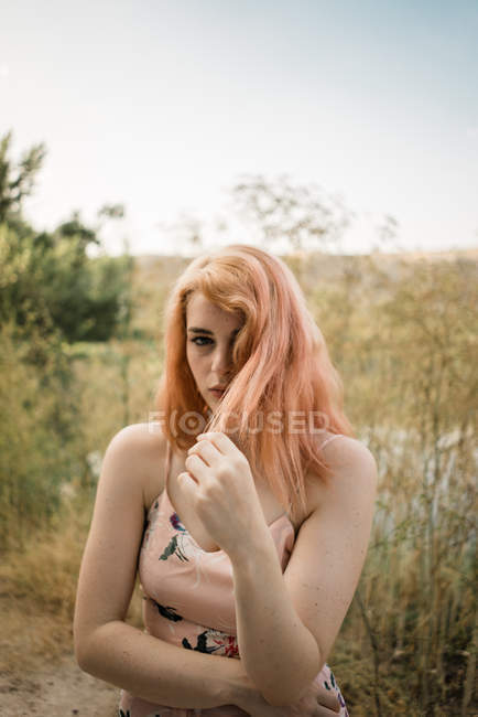 Jeune femme touchant les cheveux et posant au lac de campagne — Photo de stock