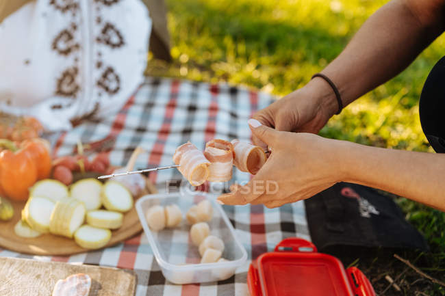 Mains humaines arrangeant des bandes de bacon pliées sur une brochette en métal pour le repas barbecue — Photo de stock