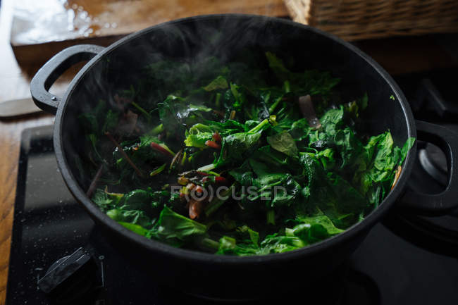 Cooking spinach leaves in pot on gas stove — Stock Photo