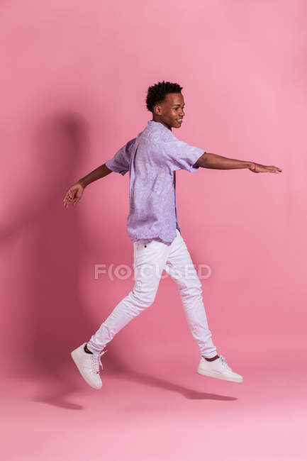 Jeune homme noir souriant en denim blanc et chemise sautant sur fond rose — Photo de stock