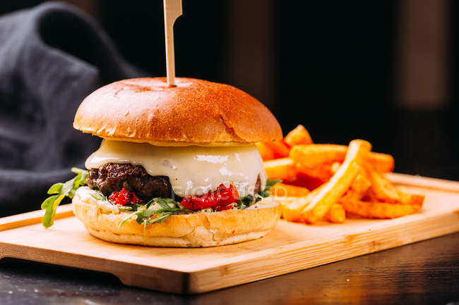Close-up de hambúrguer fresco com carne e legumes colocados em tábua de madeira com batatas fritas em tábua de madeira — Fotografia de Stock