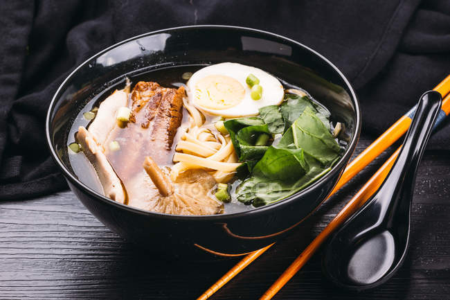 Bowl of delicious ramen on black wooden tabletop with chopsticks and ceramic spoon — Stock Photo