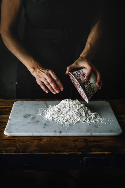 Обрезанный снимок женщины, наливающей кучу муки на мраморную доску во время приготовления пищи — стоковое фото