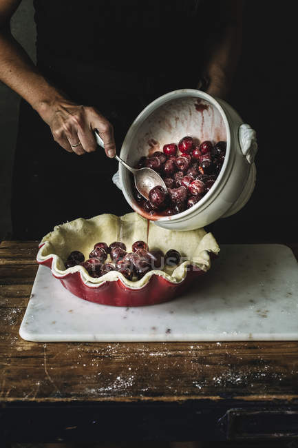 Cropped shot of woman making sweet pie and adding cherries into form with pie pastry — Stock Photo