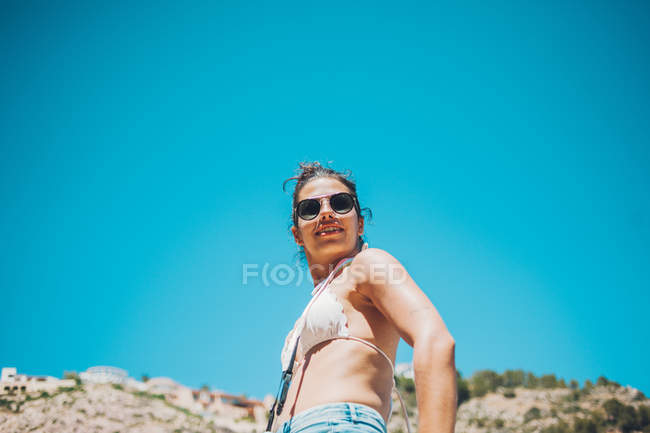 Молода дівчина стоїть перед скелястим скелею і блакитним небом — стокове фото