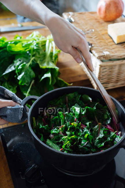 Mão humana mexendo folhas de espinafre em panela no fogão a gás — Fotografia de Stock