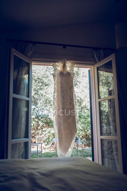 Wedding dress hanging on window curtain — Stock Photo