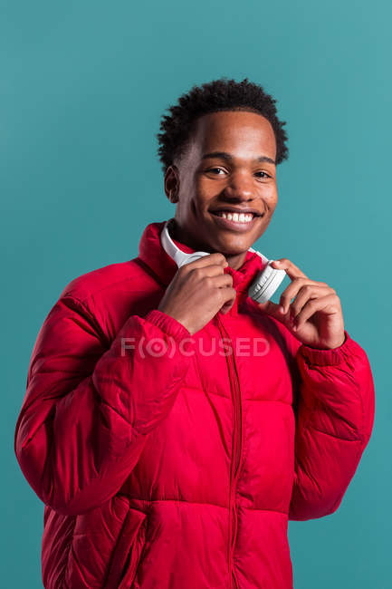 Trendy man in red puffy jacket and headphones on blue background — Stock Photo
