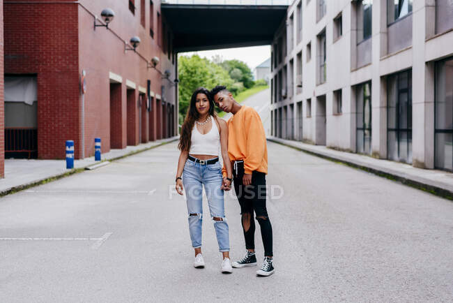 Ethnique fille et garçon adolescents tenant la main et regardant la caméra dans la rue — Photo de stock