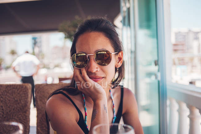 Молодая женщина в солнечных очках, сидящая летом в кафе — стоковое фото