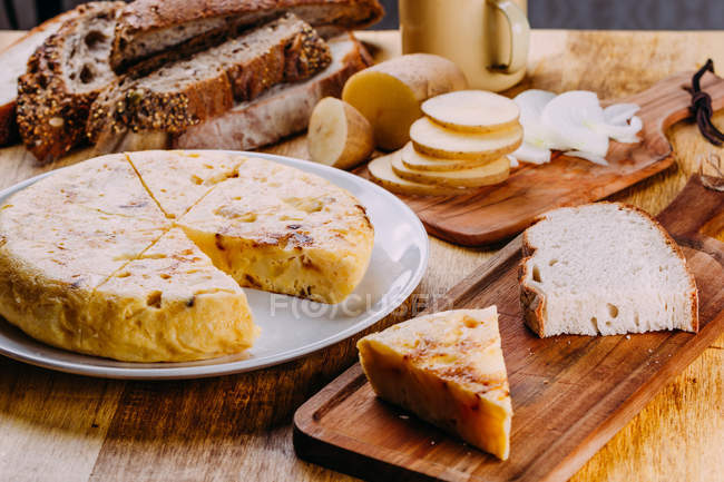 Frisch geschnittener Kuchen auf Teller auf Holztisch mit Schneidebrettern, Brot und Gemüsescheiben — Stockfoto