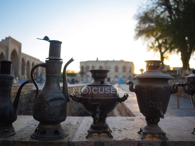 Old craft fire pots in oriental style arranged on fence with beautiful cityscape in sunset light on background, Uzbekistan — Stock Photo