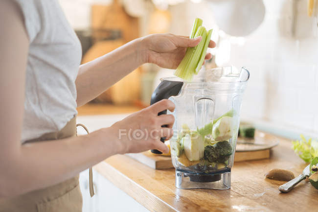 Женские руки кладут сельдерей в блендер для зеленого смузи — стоковое фото