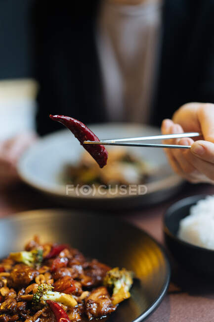 Крупный план женщины с палочками для еды, показывающими вкусный острый красный перец чили — стоковое фото