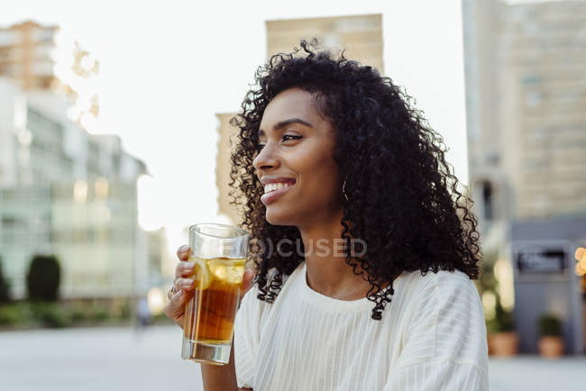 Charming African-American woman holding glass of beverage in outdoor cafe — Stock Photo