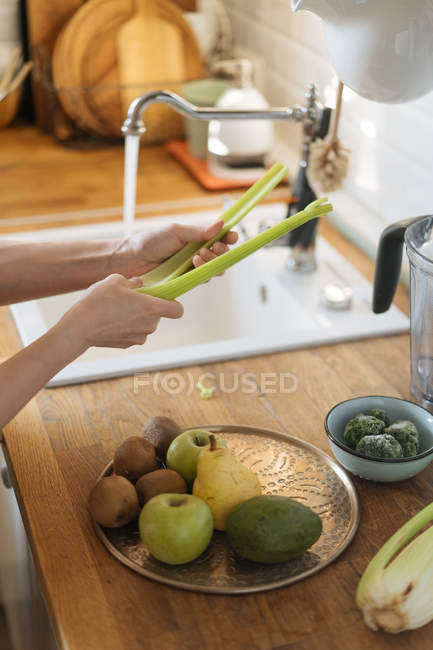 Manos femeninas lavando verduras verdes en el fregadero bajo la corriente de agua en la cocina - foto de stock