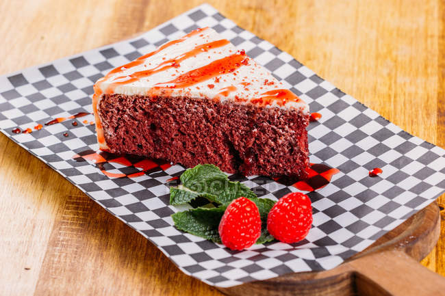 Sweet chocolate tart slice served with sauce and raspberries on checkered napkin — Stock Photo