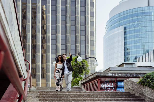 Smiling elegant couple walking down stairs together on city street — Stock Photo