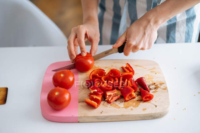 Female hands cutting red peppers and tomatoes on chopping board — Stock Photo