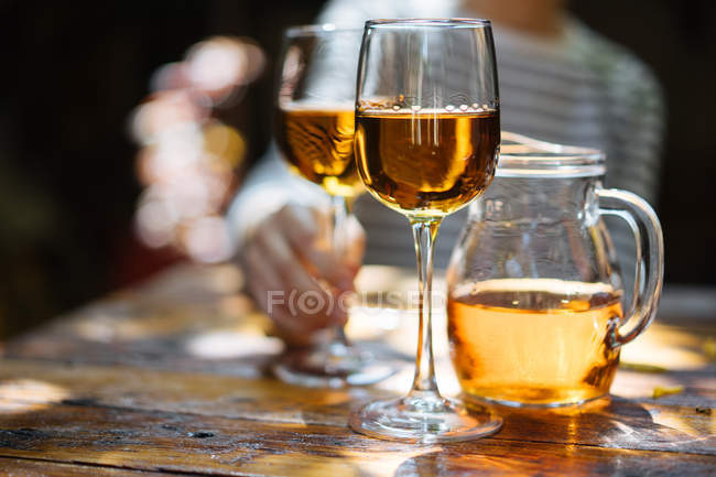 Main humaine tenant un verre de vin blanc sur une table en bois à l'extérieur — Photo de stock