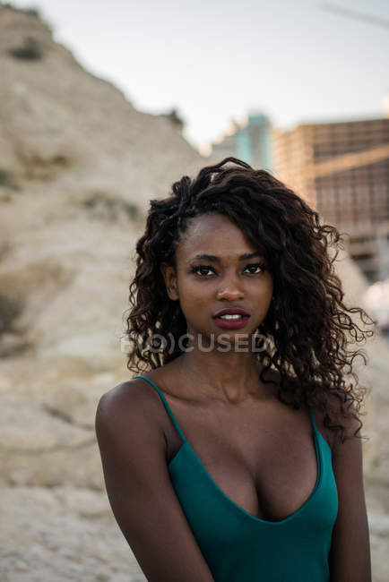 Retrato de mujer negra con el pelo rizado de pie en la orilla de la ciudad - foto de stock
