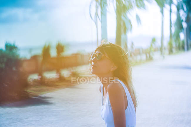 Woman in sunglasses sitting on bench in tropical park — Stock Photo