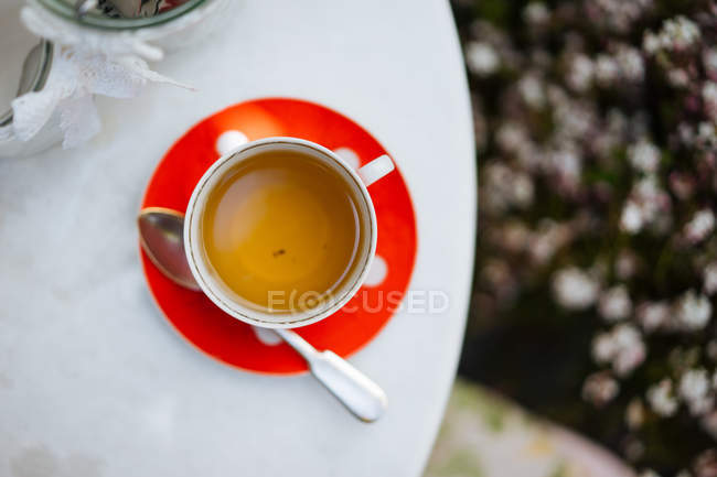 Taza de té de lunares de cerámica roja en platillo en mesa de jardín - foto de stock