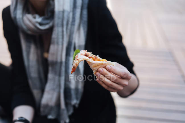 Close-up of female hand holding piece of pizza outdoors — Stock Photo