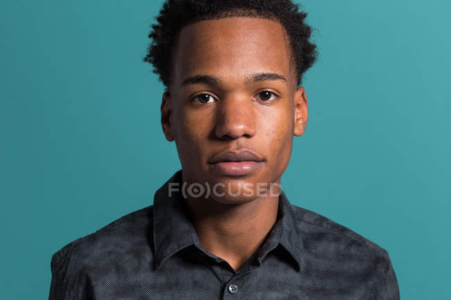 Retrato de un joven afroamericano serio con camisa sobre fondo azul - foto de stock