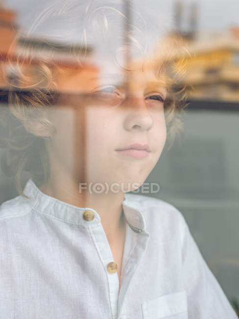 Сумний хлопчик дивиться через скло. — стокове фото