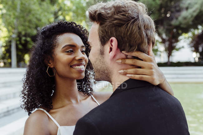 Attractive woman smiling looking at man while standing in park and touching his neck — Stock Photo