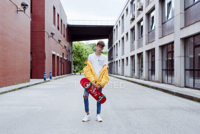 Adolescente com skate em pé na rua — Fotografia de Stock