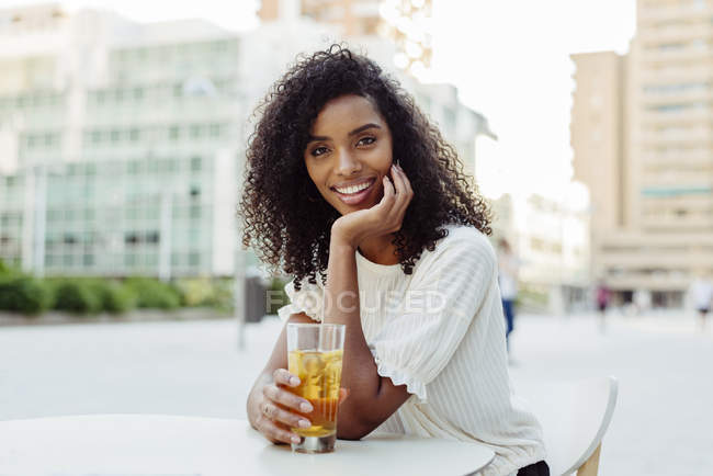 Affascinante donna afro-americana che tiene un bicchiere di bevanda in un caffè all'aperto — Foto stock