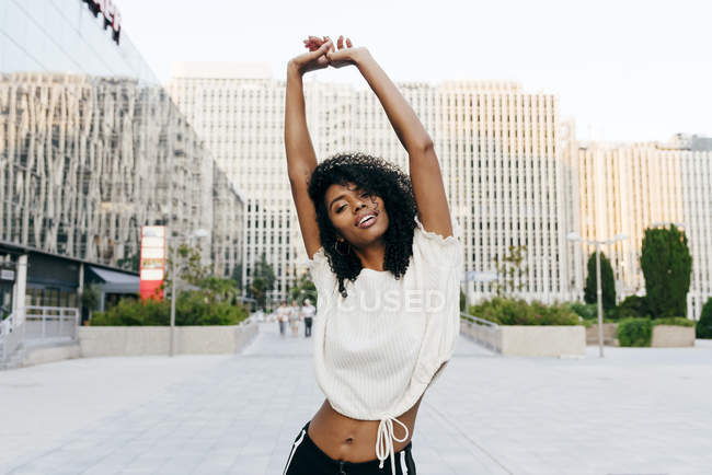 Riendo mujer afroamericana de pie en la calle con las manos en alto y mirando a la cámara - foto de stock