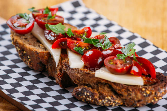 Braunes Brotsandwich mit Käse und Tomaten auf karierter Serviette — Stockfoto