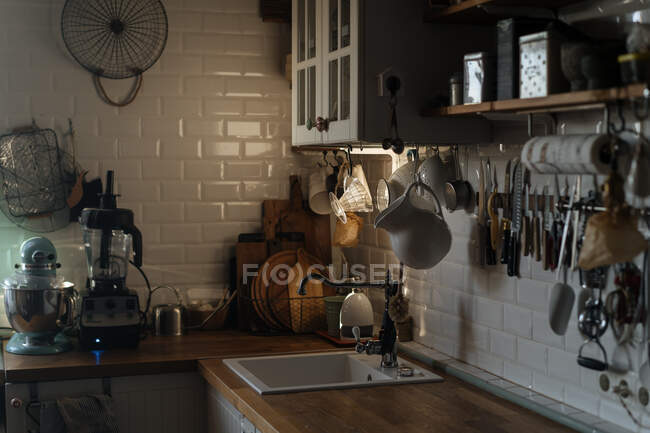 Interior of kitchen with white tiled walls and plenty of utensil and appliance composed on shelves and countertop — Stock Photo