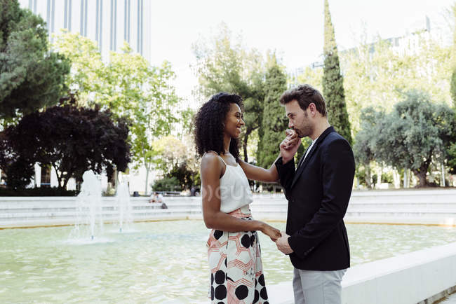 Мужчина целует подружку руку возле фонтана в парке — стоковое фото