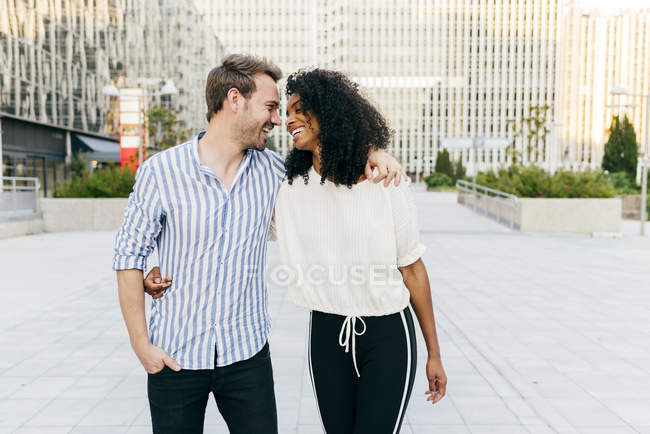 Cheerful multiracial couple hugging and laughing while walking on city street together — Stock Photo