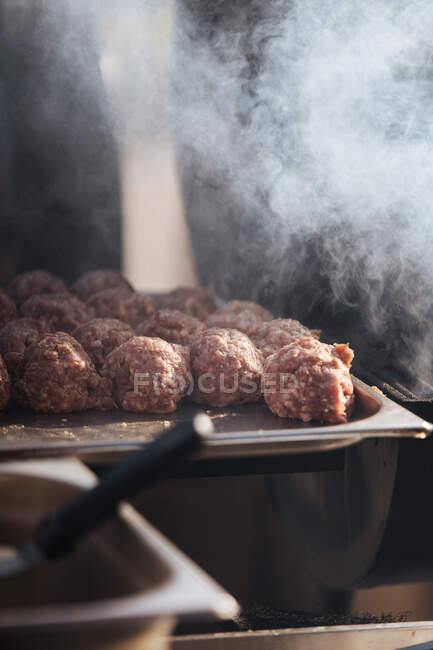 Palle di carne cruda composte su vassoio metallico per polpette hamburger in fumo di griglia — Foto stock