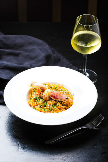 Traditional italian risotto with shrimps on white ceramic plate with glass on white wine on dark background — Stock Photo