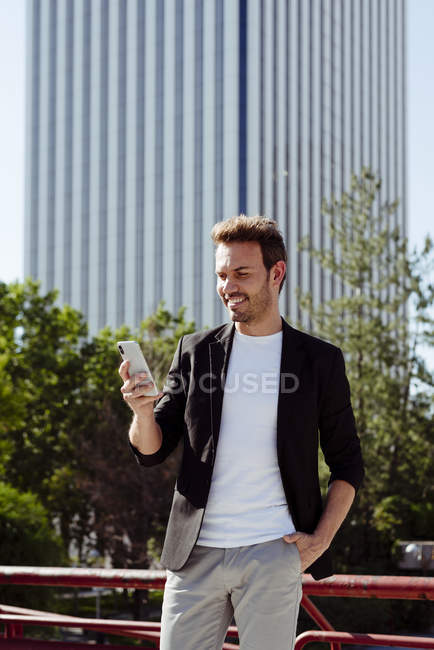 Cara elegante usando smartphone enquanto se inclina no corrimão na rua da cidade moderna — Fotografia de Stock