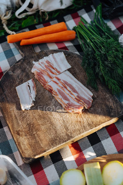 Plaid with board and served bacon among fresh peeled vegetables for picnic cooking — Stock Photo