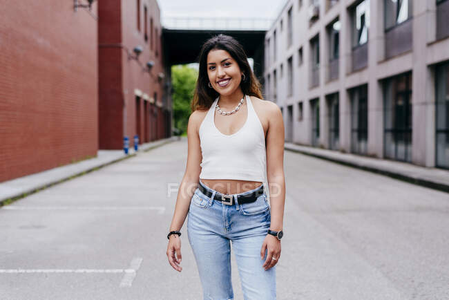 Cheerful young woman in casual clothes smiling and looking at camera on urban street — Stock Photo