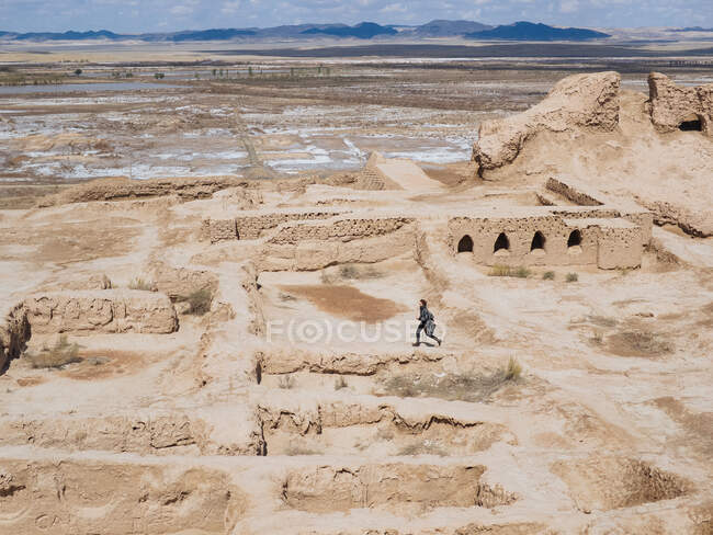 Side view of man running on remnants of ancient stone building in endless dry terrain of Uzbekistan — Stock Photo