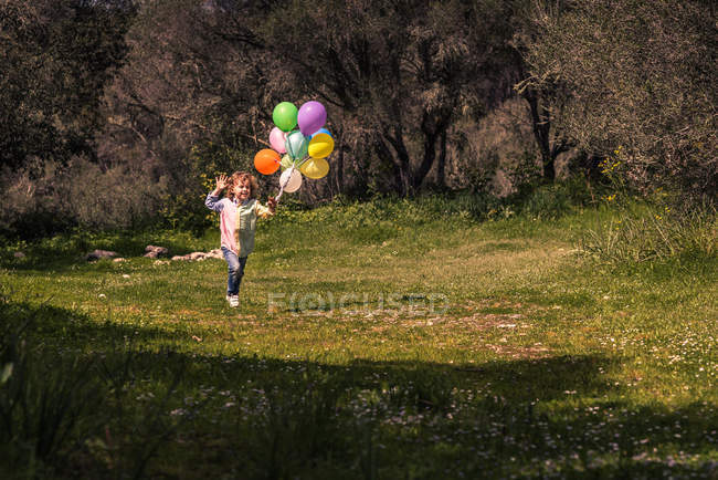 Хлопчик початкового віку біжить на лузі з повітряними кулями — стокове фото