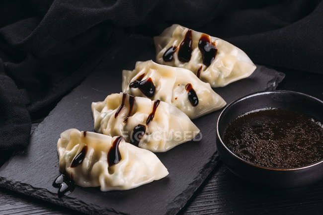 Deliziosi gnocchi di cucina asiatica su ardesia e ciotola di salsa di soia — Foto stock