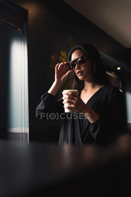 Брюнетка жінка в сонцезахисні окуляри, проведення папір чашку кави — стокове фото
