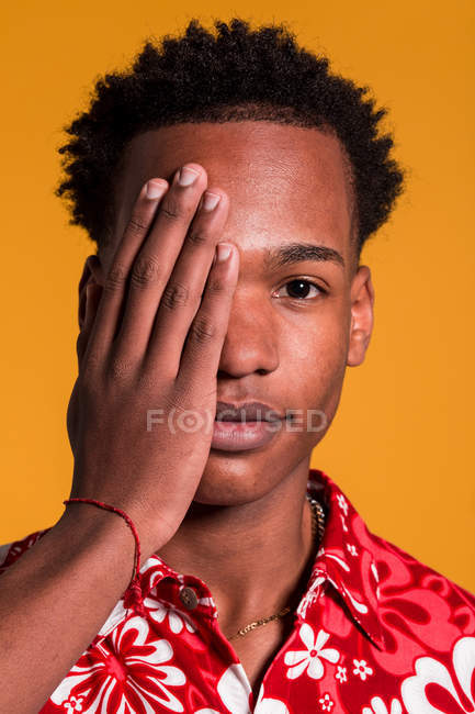 Stylischer, fröhlicher Mann im Strandhemd, der Auge mit Hand auf orangefarbenem Hintergrund bedeckt — Stockfoto