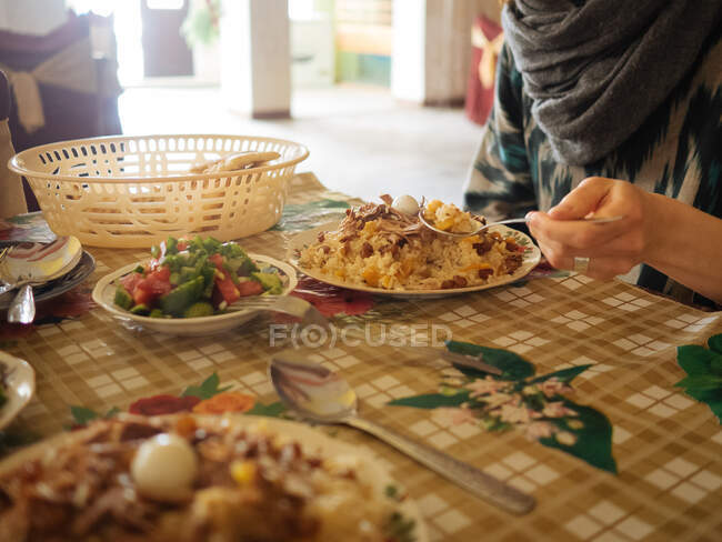 Tiro sem rosto de mulher tentando prato tradicional de pilaf à mesa com salada fresca, Uzbequistão — Fotografia de Stock